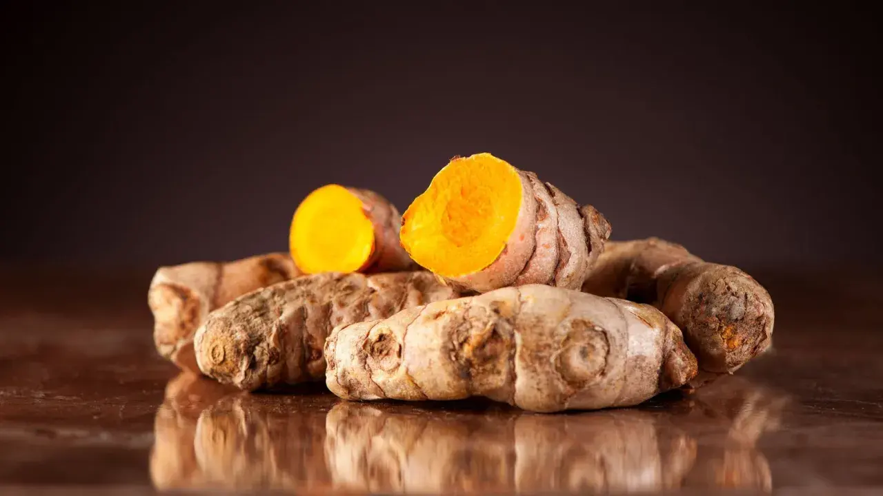 Ein Haufen ganzer und halber Kurkumawurzeln. Man sieht, wie sieht kurkuma aus: außen braun und innen leuchtend orange.