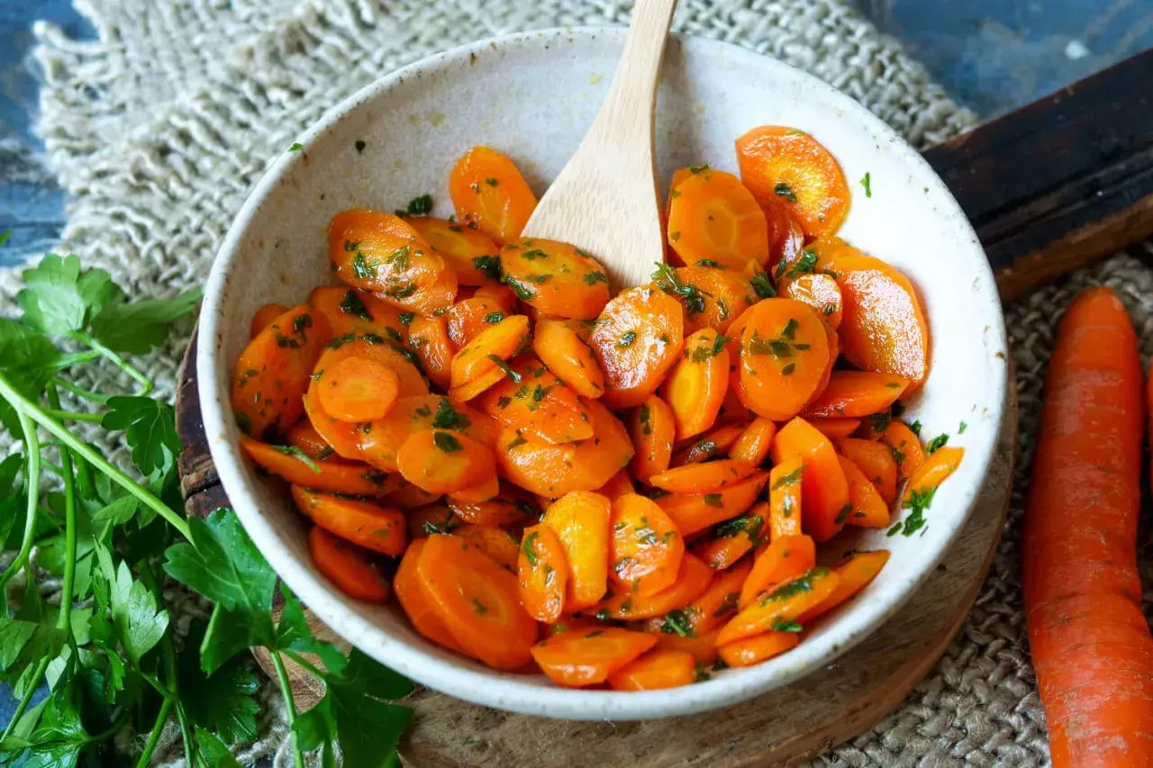 Schmackhafte Karotten-Rezepte: Glasierte Karotten mit Petersilie in einer Schüssel, daneben frische Karotten.