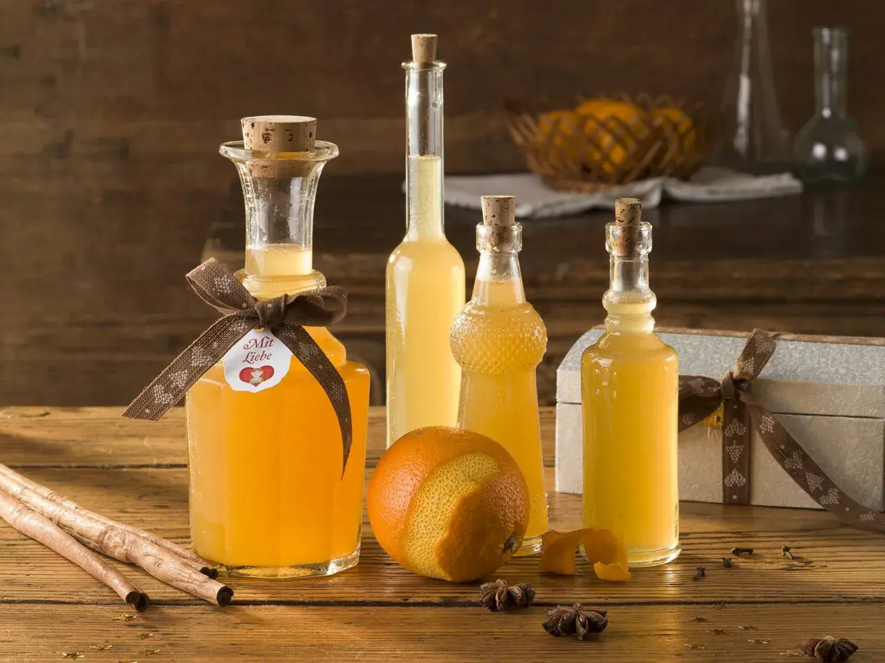 Flaschen mit selbstgemachtem Schnaps, Orangen, Zimtstangen und Sternanis auf Holztisch.