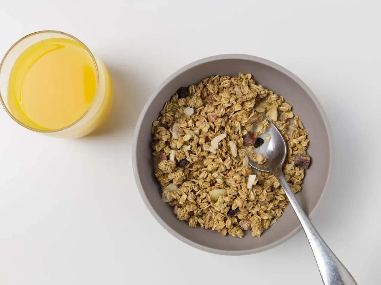 Schüssel mit dinkelflocken oder haferflocken, Nüssen und Trockenfrüchten, daneben ein Glas Orangensaft.
