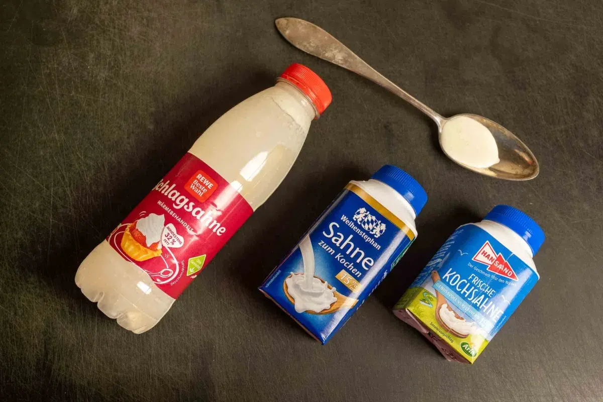 Drei Packungen Sahne zum Backen und Kochen liegen neben einem Löffel mit Sahne.