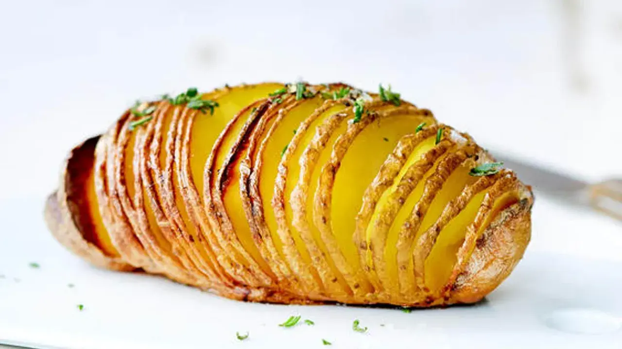 Eine goldbraune Hasselback Kartoffel, knusprig und mit frischen Kräutern bestreut, wartet darauf, genossen zu werden.