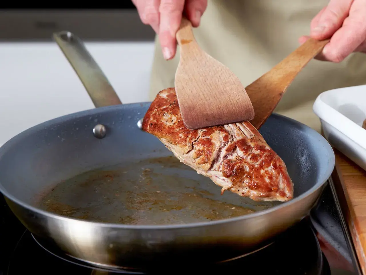 Ein saftiges Schweinefilet wird mit zwei Holzspateln in einer Pfanne gewendet, um es perfekt zu braten.