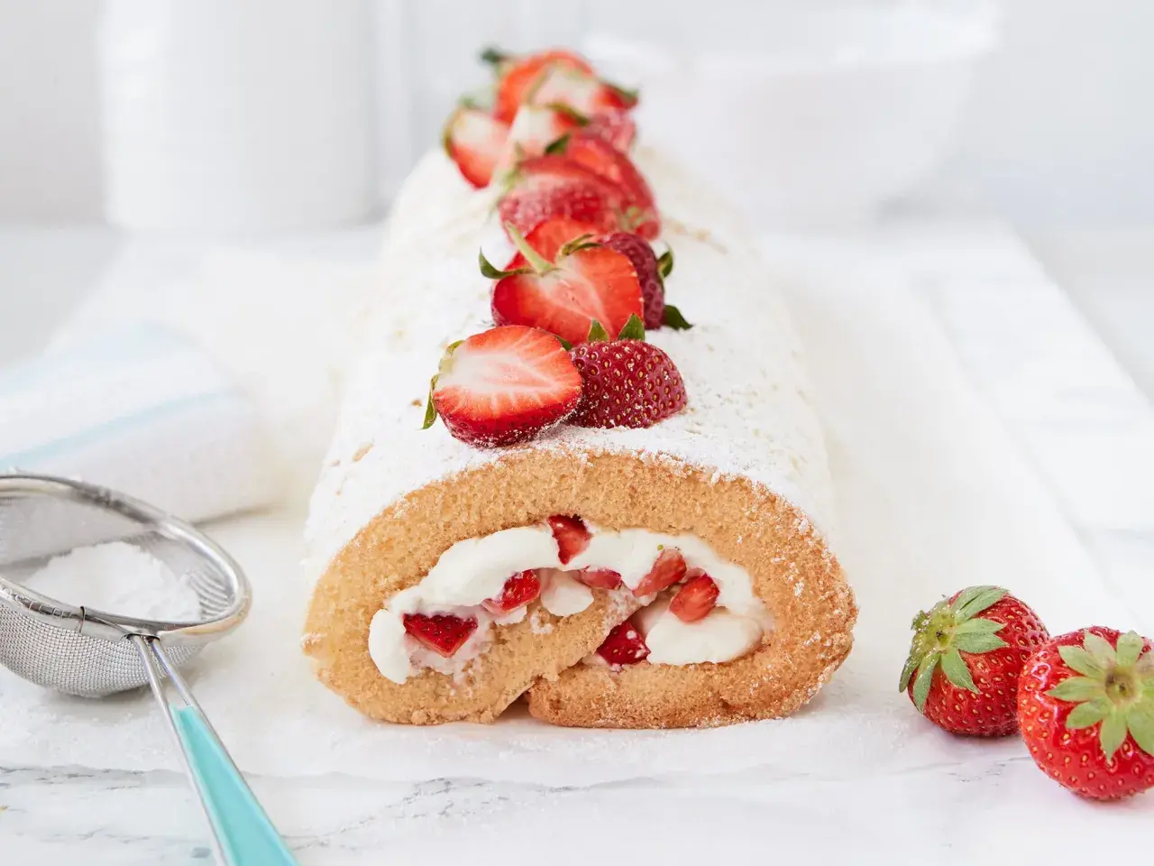 Biskuitrolle Grundrezept mit 5 Eiern, gefüllt mit Sahne und Erdbeeren, bestäubt mit Puderzucker.