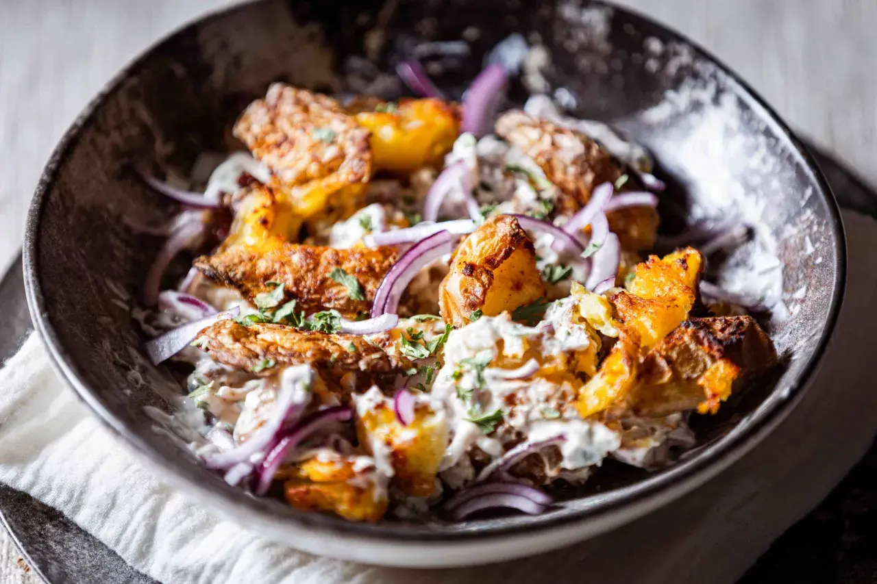 Knuspriger Kartoffelsalat mit cremiger Soße, roten Zwiebeln und frischer Petersilie in einer dunklen Schüssel.