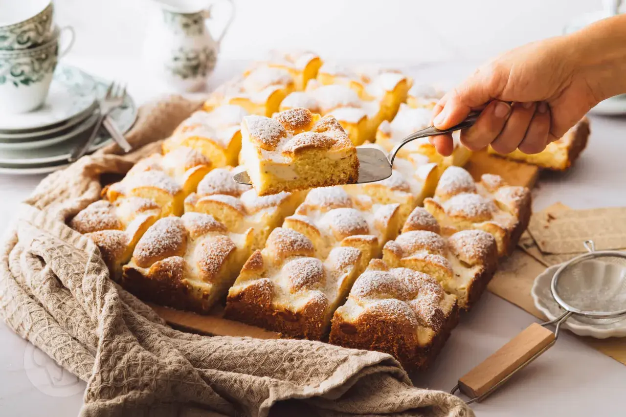 Ein Stück eines saftigen Blechkuchens mit Puderzucker wird herausgehoben. Perfekt für schnelle Blechkuchen Rezepte.