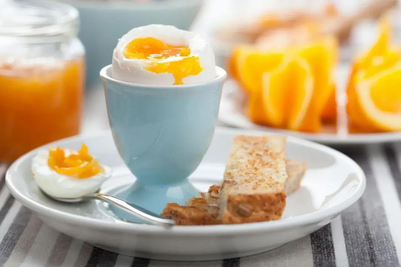 Ein perfekt gekochtes Ei im Wasserkocher, serviert mit Toast und Orangenspalten.