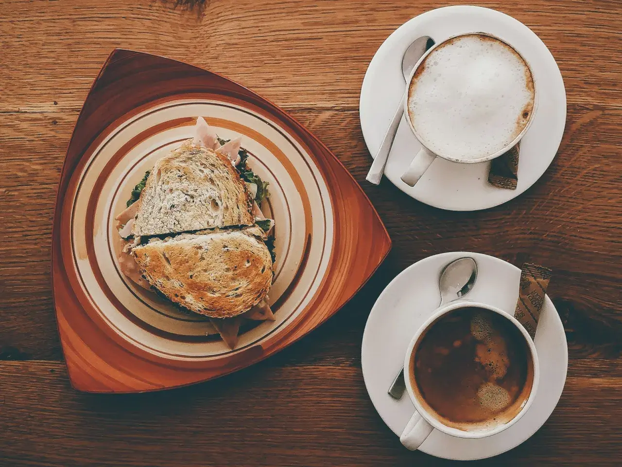 Ein Sandwich und zwei Kaffees auf einem Holztisch. Der Kaffee könnte mit Kaffeesirup verfeinert werden.