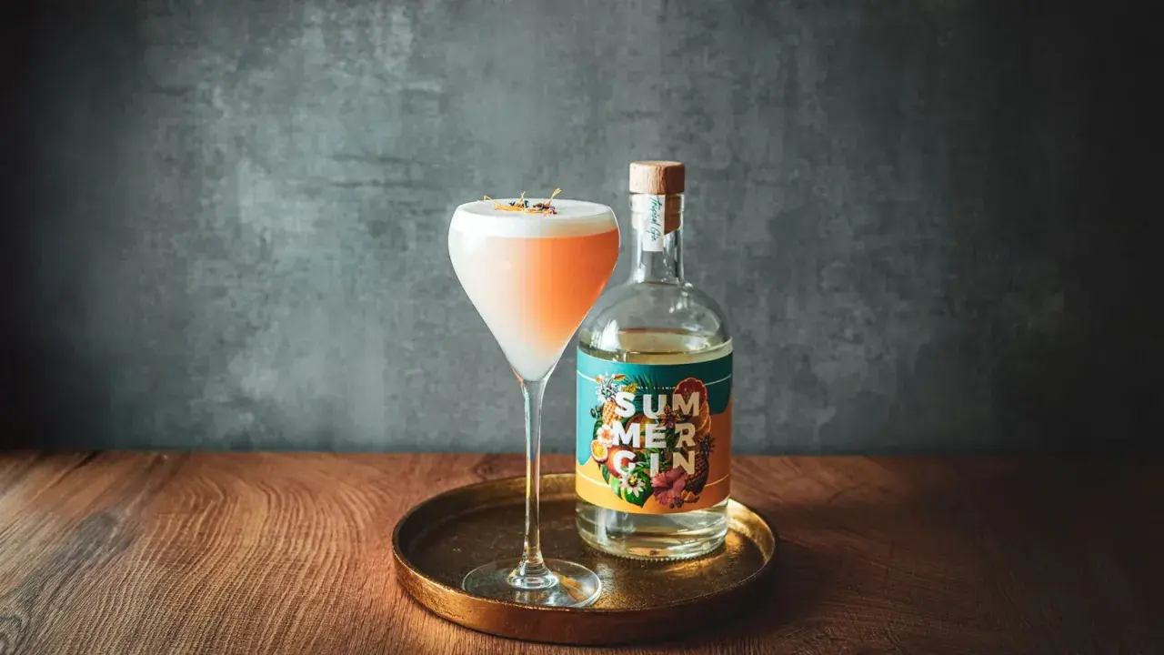 Ein erfrischender Gin-Cocktail mit cremigem Schaum und einer Flasche "Summer Gin" daneben. Perfekt für warme Tage.