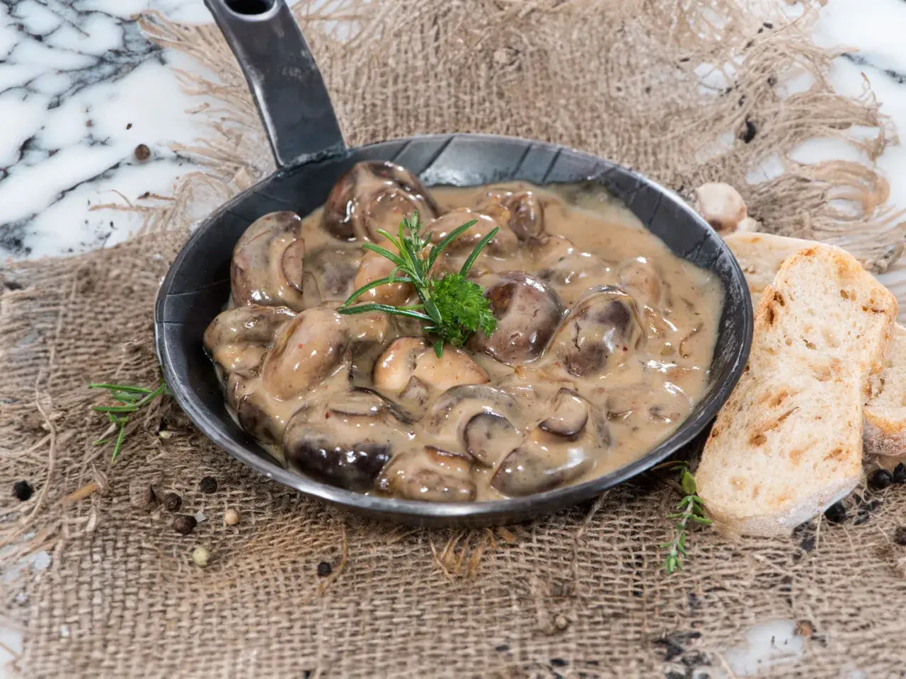 Herzhafte Champignon Rahmsauce in einer Pfanne, garniert mit Rosmarin, serviert mit knusprigem Brot.