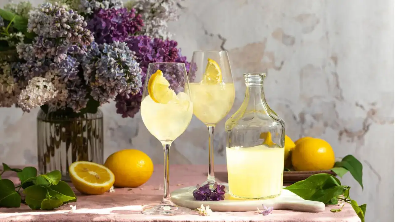 Erfrischender Limoncello Spritz mit Zitrone und Eis, dekoriert mit Flieder.