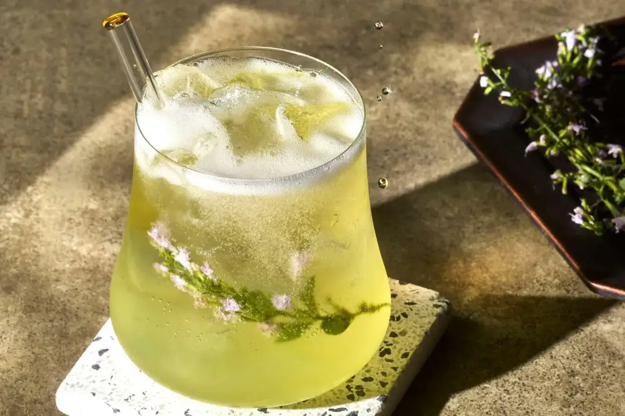 Erfrischender Limoncello Spritz mit Eis, Kräutern und einem Glasstrohhalm.