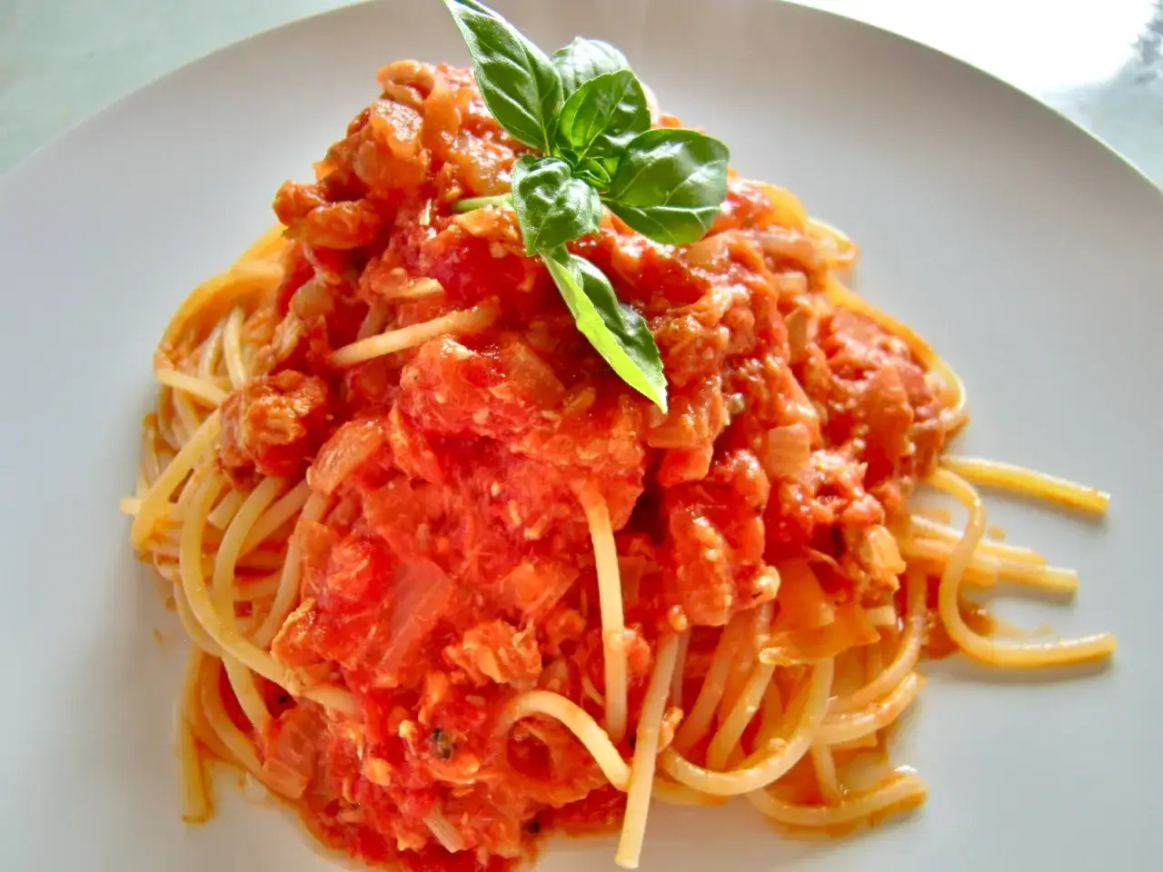 Ein Teller Spaghetti mit einer reichhaltigen Sauce aus Lachs und Tomaten, garniert mit frischem Basilikum.