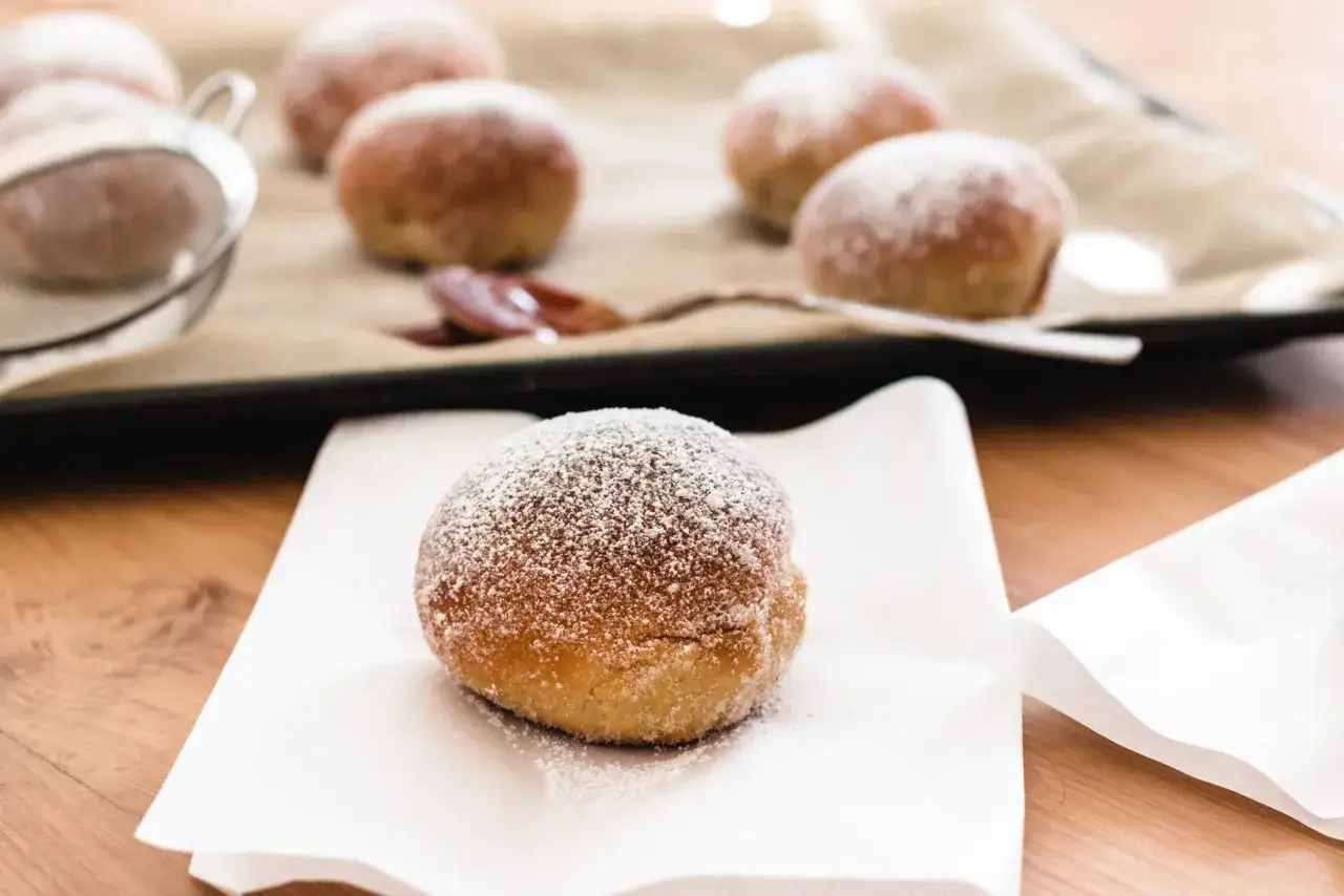 Frisch zubereitete berliner im airfryer, mit Puderzucker bestäubt, liegen auf einem Backpapier.