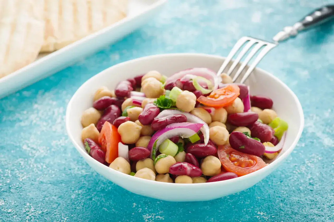 Bunter Bohnensalat mit Kichererbsen, Tomaten und Zwiebeln, inspiriert von einfachen Bohnensalat Rezepten. Eine Gabel wartet auf den ersten Bissen.