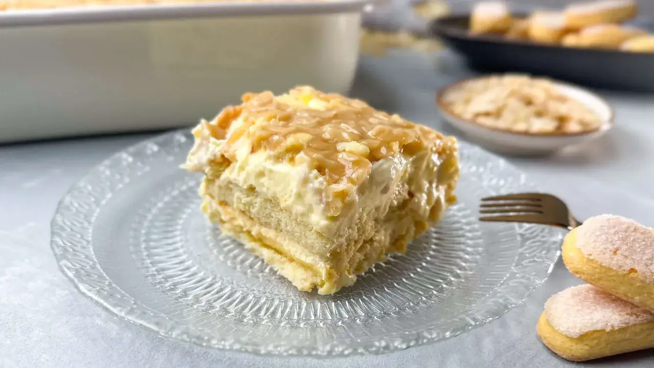 Ein St&uuml;ck Bienenstich mit Mandelkruste, ohne backen, auf einem Glas-Teller. Cremig und mit knuspriger Mandelkruste.