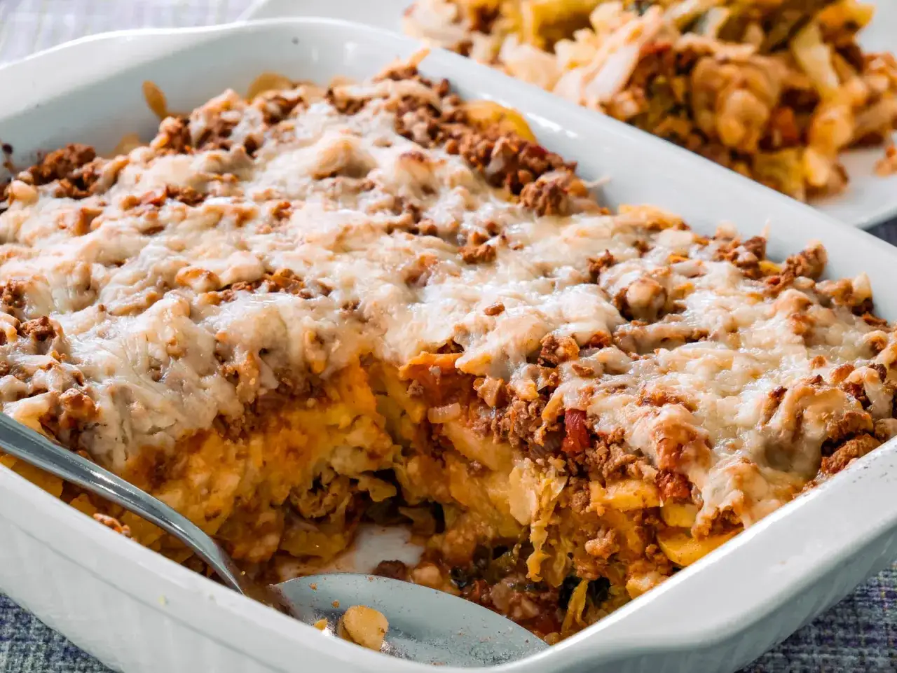Omas Kartoffelauflauf mit Hackfleisch, &uuml;berbacken mit geschmolzenem K&auml;se. Ein L&ouml;ffel ist bereits hineingesteckt, bereit zum Servieren.