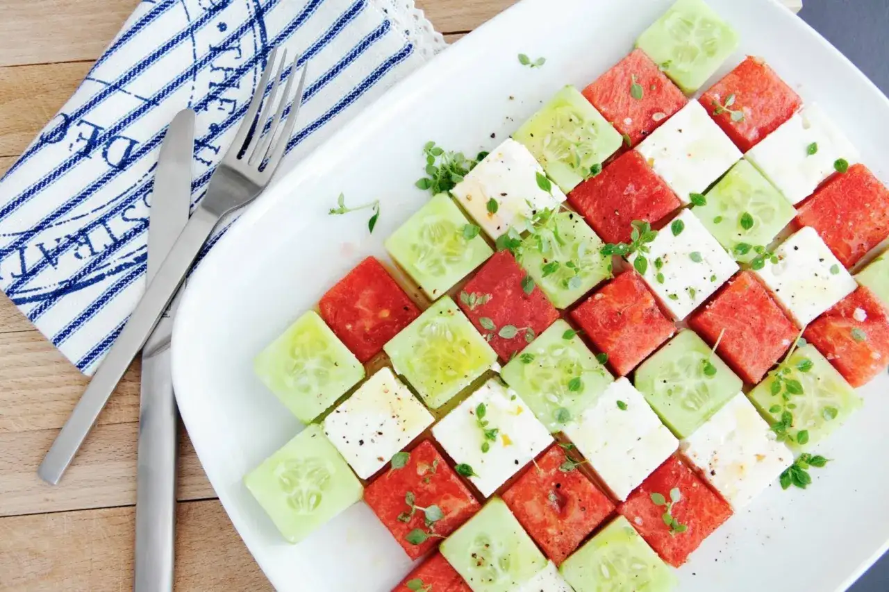 Erfrischender Salat mit Melone, Gurke und Feta, kunstvoll auf einer Platte arrangiert, garniert mit frischen Kräutern.
