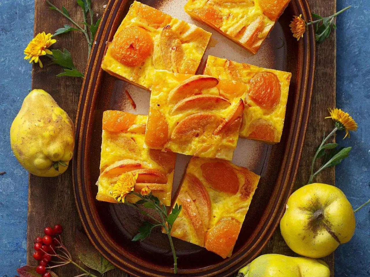 Süßer Kuchen mit Quittenfrucht-Stücken und ganzen Quitten daneben.
