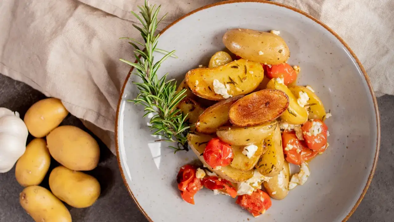K&ouml;stliche Drillinge kochen mit Rosmarin, Kirschtomaten und Feta. Daneben liegen rohe Kartoffeln und Knoblauch.