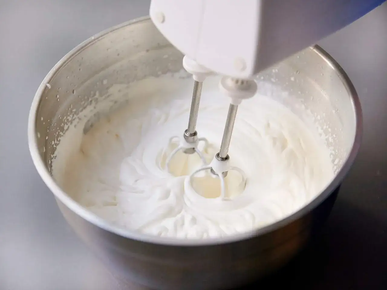Schlagrahm wird mit einem Handmixer in einer Edelstahlsch&uuml;ssel aufgeschlagen. So einfach l&auml;sst sich Sahne steif selber machen f&uuml;r Kuchen und Desserts.