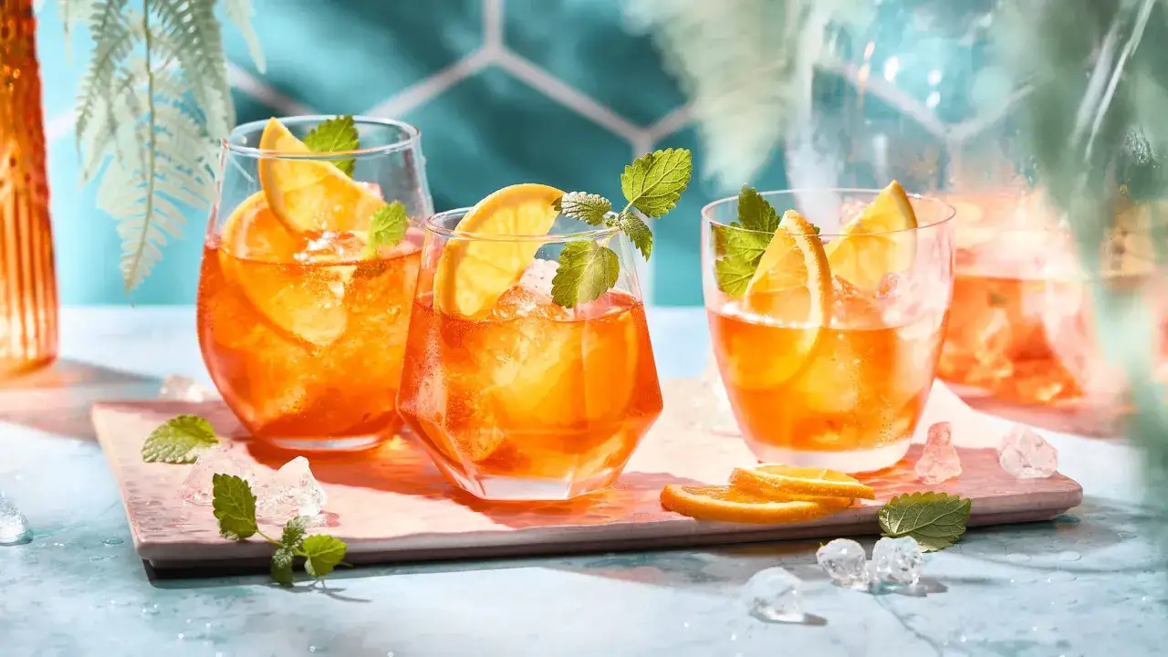 Erfrischende Aperol Bowle mit Orangen und Minze, serviert mit Eisw&uuml;rfeln auf einem rosa Brett. Perfekt f&uuml;r einen sonnigen Nachmittag.