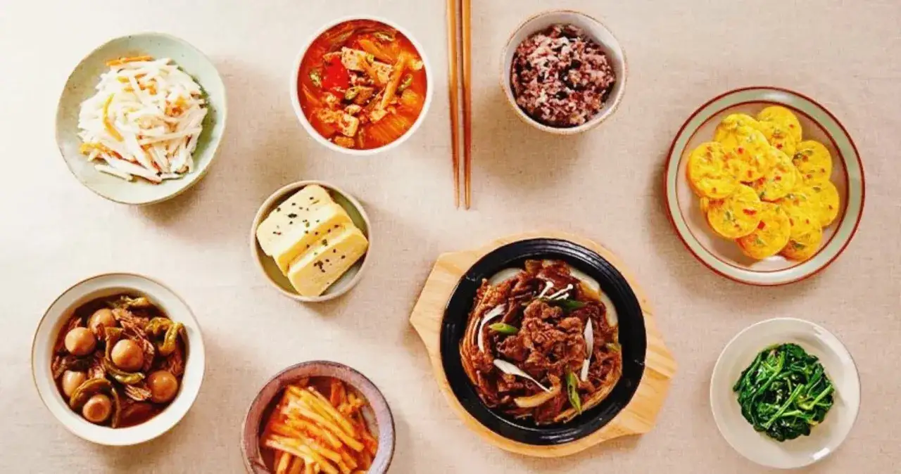 Ein Tisch voller koreanischer K&ouml;stlichkeiten: Gulasch, Reis, Kimchi und verschiedene Beilagen.