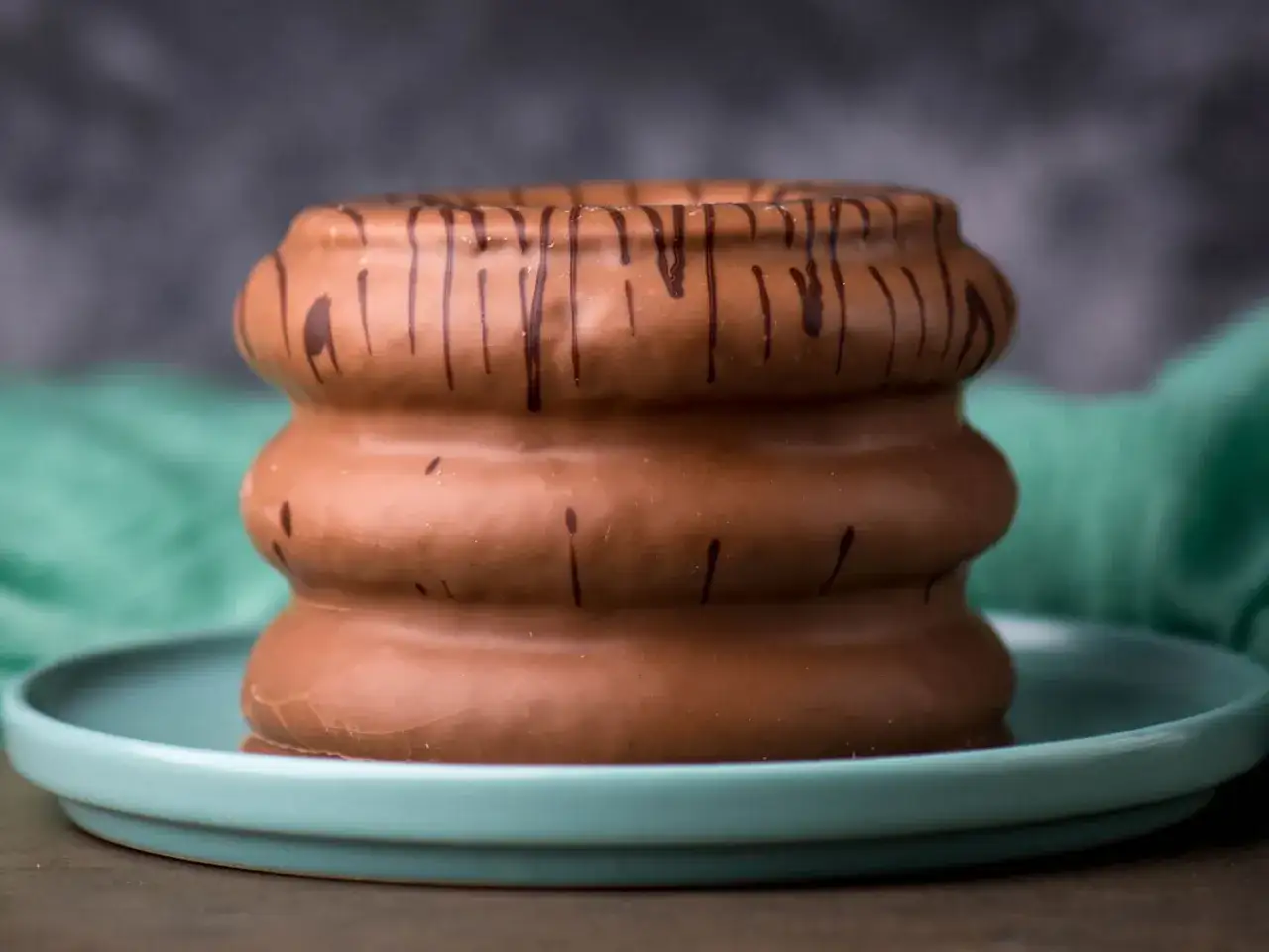 Schokoladen&uuml;berzogener Baumkuchen, ein Meisterwerk der Baumkuchen Herstellung, ruht auf einem t&uuml;rkisfarbenen Teller.