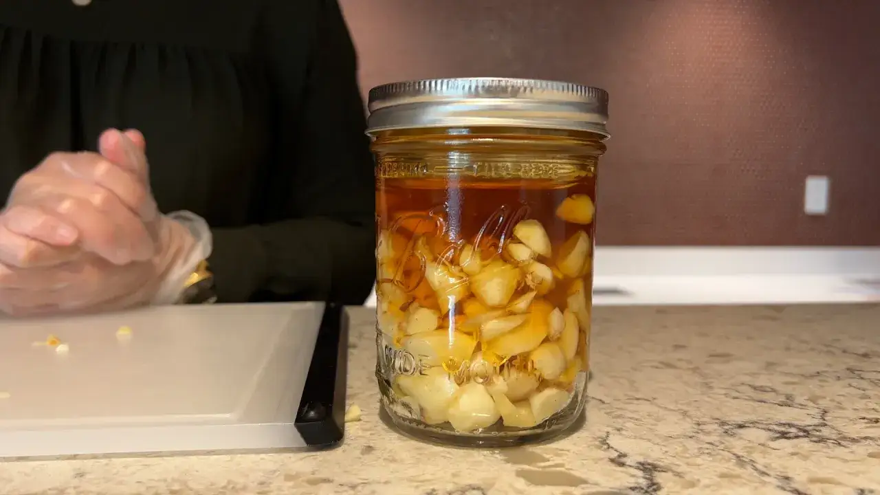 Ein Glas mit Zwiebeln, Honig und Saft. Die Zwiebeln sind in einer goldenen Fl&uuml;ssigkeit eingelegt, die wie Honig aussieht.