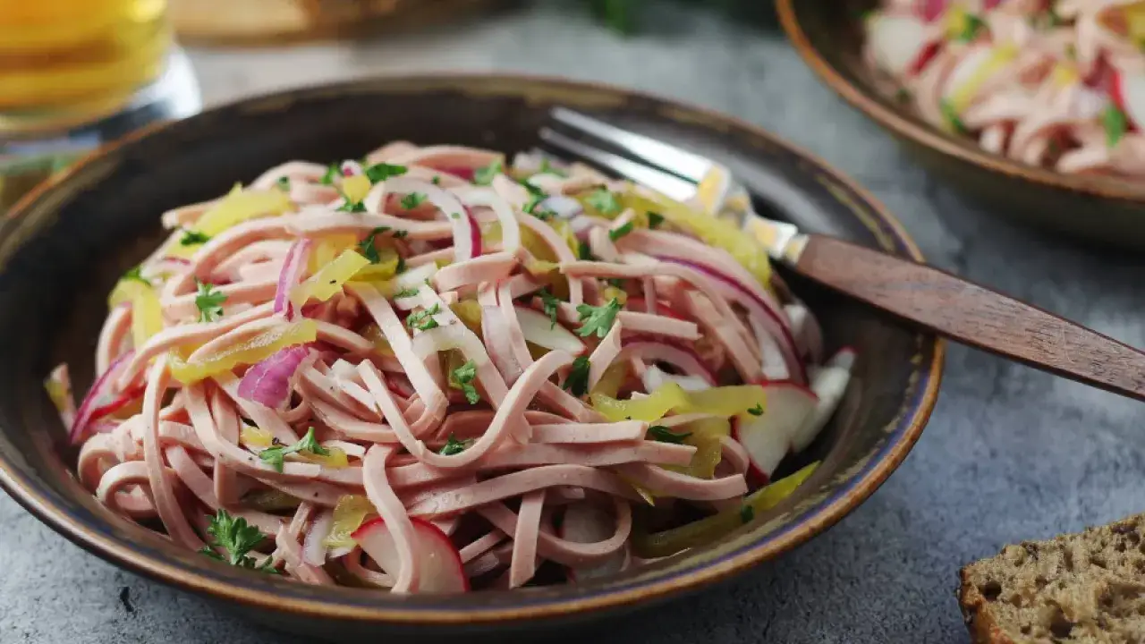 Bayerischer Wurstsalat, frisch zubereitet mit Wurststreifen, Zwiebeln, Radieschen und Petersilie, serviert in einer rustikalen Sch&uuml;ssel.