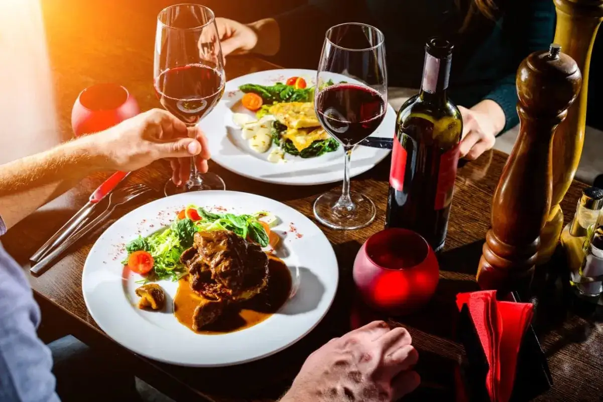 Ein romantisches Essen zuhause: Zwei Teller mit köstlichem Essen, Rotwein und Kerzenlicht schaffen eine intime Atmosphäre.