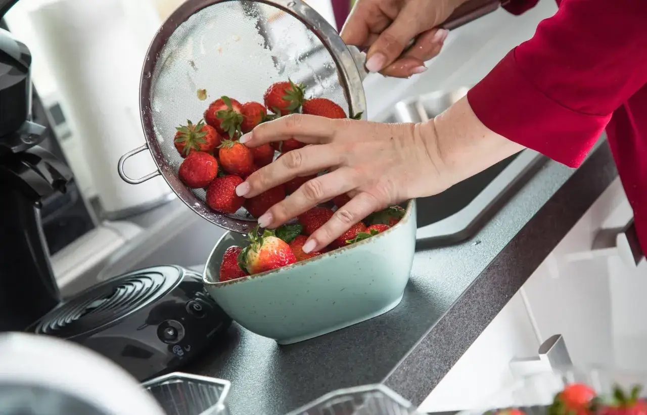 H&auml;nde waschen Erdbeeren in einer Sch&uuml;ssel. Frische rote Fr&uuml;chte werden aus einem Sieb in eine hellblaue Schale gegeben.