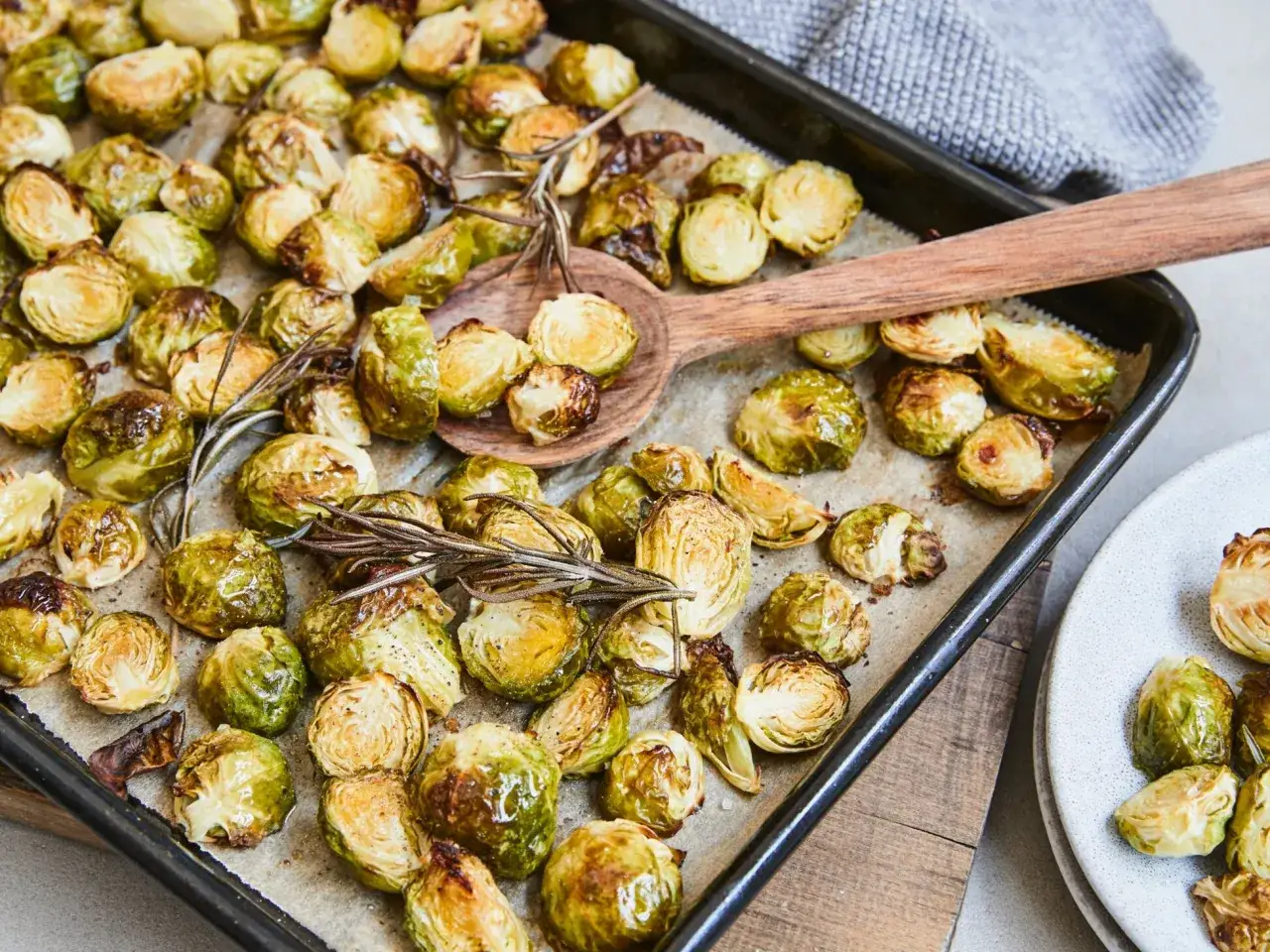 Gerösteter Rosenkohl mit Rosmarin, eine köstliche Beilage zu Fleisch, liegt auf einem Backblech.