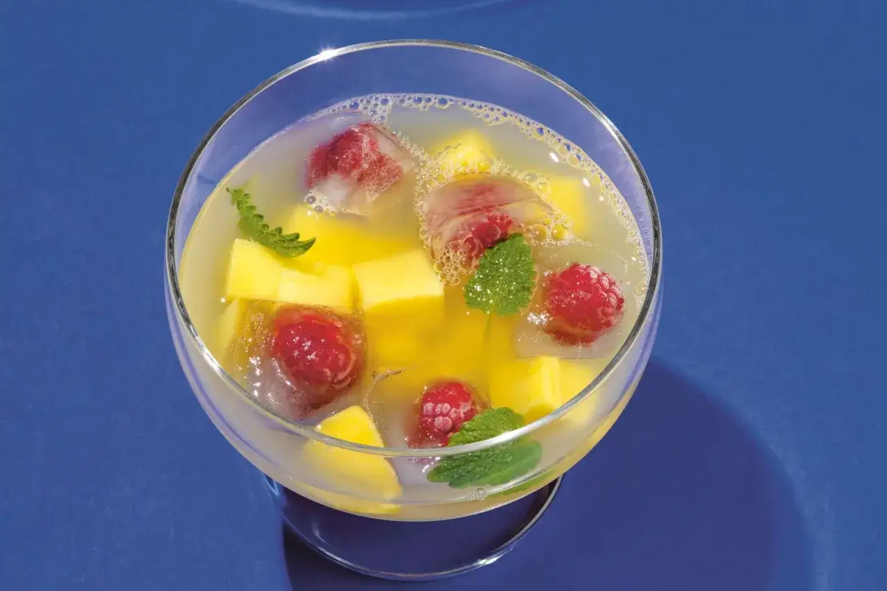 Erfrischende alkoholfreie Bowle mit Mango, Himbeeren und Minze in einem Glas.