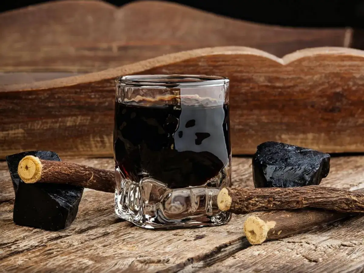 Glas mit dunklem Lik&ouml;r, daneben Lakritzst&uuml;cke und -wurzeln. Perfekt, um Lakritz Schnaps selber machen zu wollen.