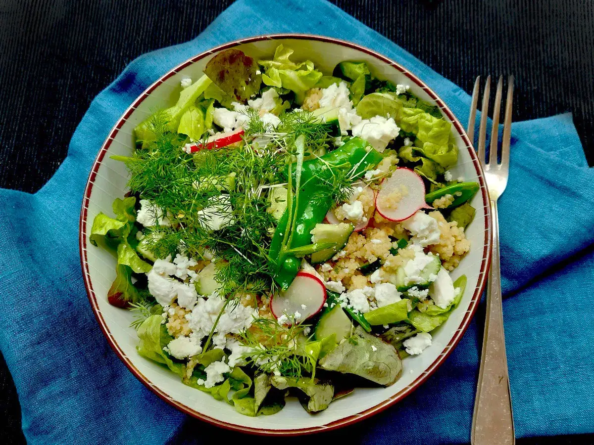 Frischer Hirse Salat mit Feta, Gurken, Radieschen und Dill auf blauem Tuch.