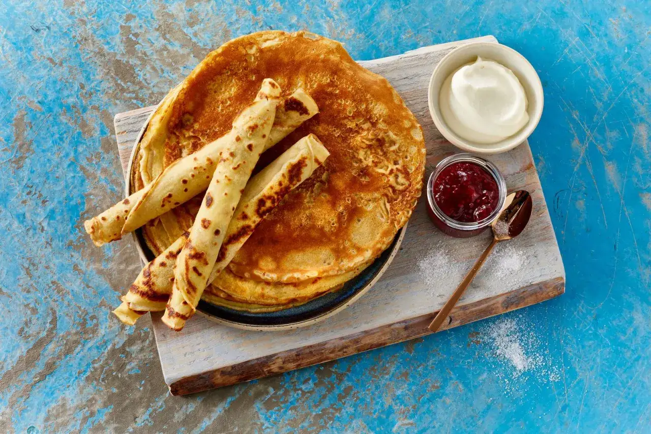 Ein Stapel goldbrauner Pfannkuchen, einige gerollt, mit Marmelade und Sahne. Ein leckeres Pfannkuchen Rezept für jeden Tag.