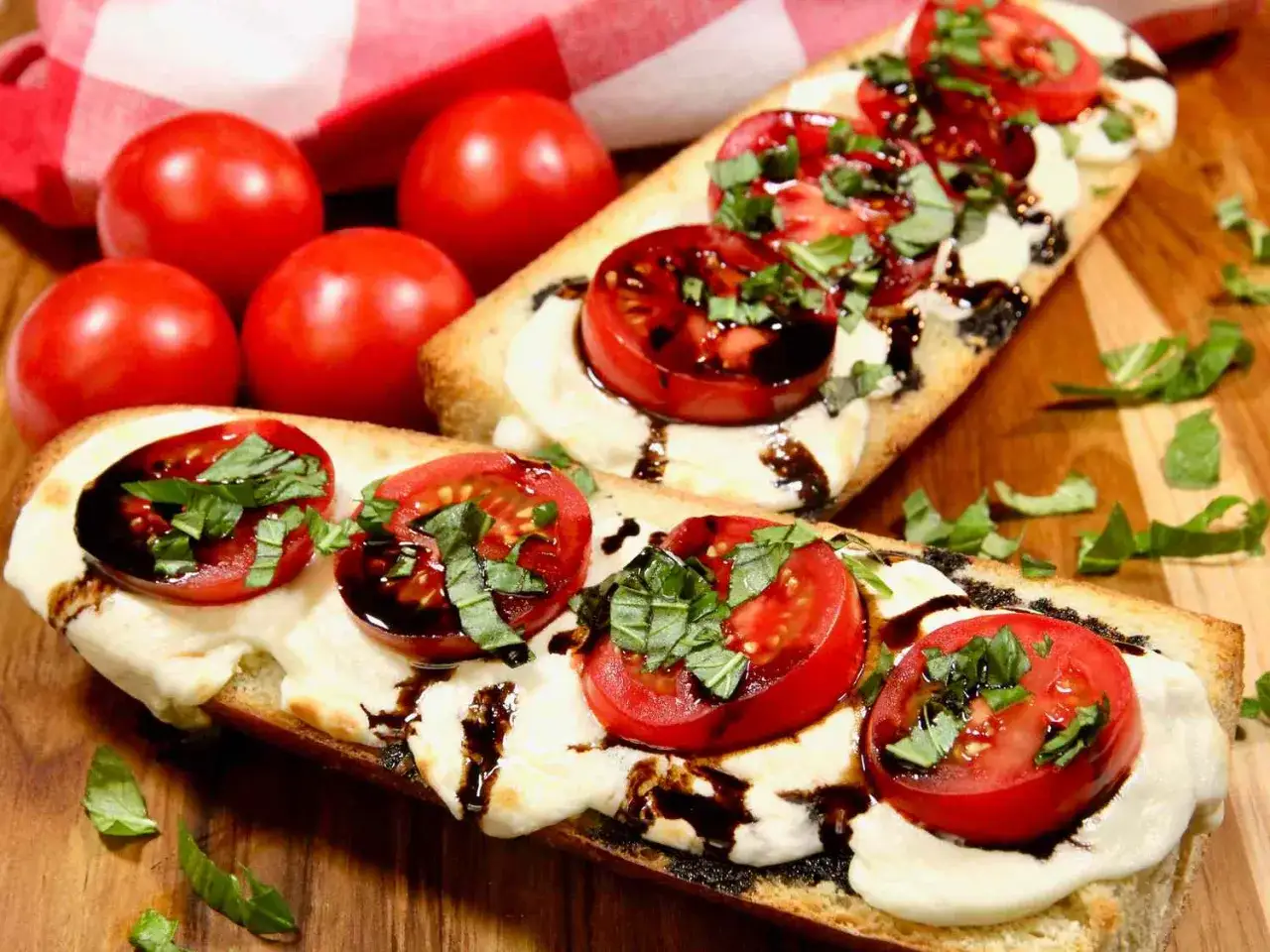 Tomate Mozzarella Aufstrich auf ger&ouml;stetem Brot mit frischem Basilikum und Balsamico-Glasur. Daneben liegen frische Tomaten.
