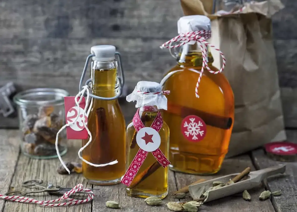 Selbstgemachter Schnaps in Flaschen mit Zimtstangen, dekoriert f&uuml;r Weihnachten. Zutaten wie Kardamom und Zucker sind daneben zu sehen.