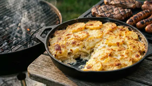 Herzhaftes Kartoffelgratin einfach mit Sahne, goldbraun gebacken, neben gegrilltem Fleisch und Würstchen.