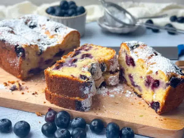 Saftiger skyrkuchen mit heidelbeeren, bestäubt mit Puderzucker. Frische Heidelbeeren liegen daneben.