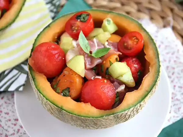 Erfrischender **Salat mit Melone**, Tomaten und Schinken, serviert in einer ausgehöhlten Honigmelone. Ein leichter Genuss!