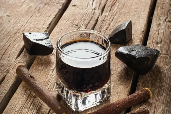 Ein Glas dunkler Flüssigkeit, umgeben von Lakritzstücken und -wurzeln. Perfekt für alle, die **Lakritz Schnaps selber machen** möchten.