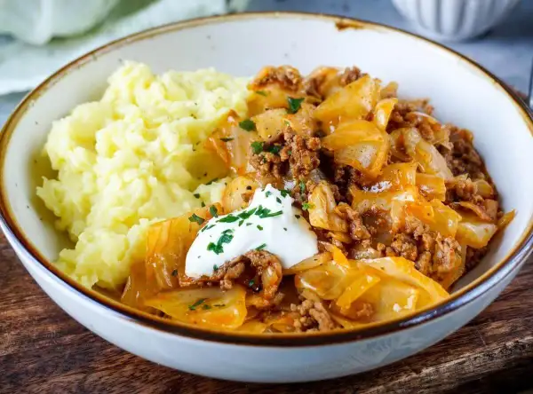 Herzhaftes Schmorkohl mit Hackfleisch, garniert mit einem Klecks Sour Cream und Petersilie, serviert mit cremigem Kartoffelpüree.