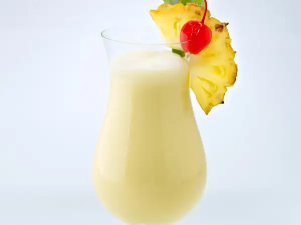 Cremiger Pina Colada mit Ananasstück und Kirsche garniert.