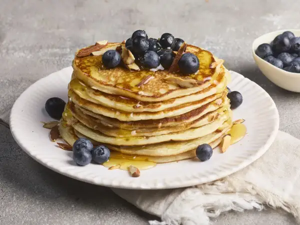 Stapel protein pancakes mit Magerquark, garniert mit Blaubeeren und Mandelsplittern, beträufelt mit Honig.