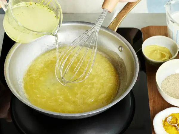 Flüssigkeit wird in eine Pfanne gegossen, während mit einem Schneebesen gerührt wird. Zutaten für eine vegane Sauce Hollandaise werden vorbereitet.