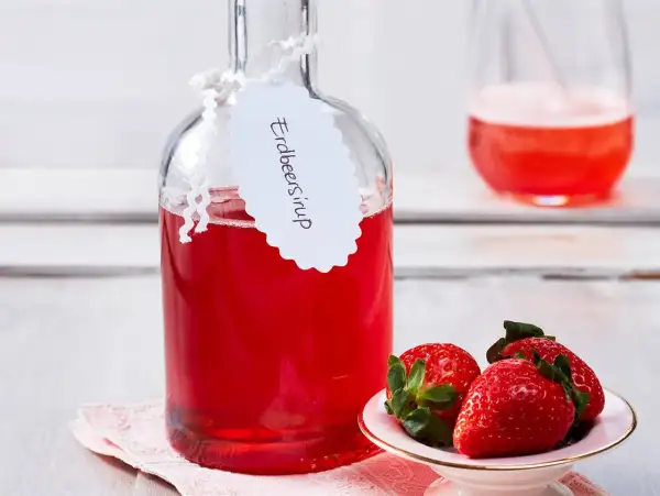 Flasche mit selbstgemachtem Erdbeersirup, garniert mit frischen Erdbeeren. Perfekt für Cocktails oder als Topping.