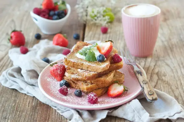 Ein Stapel goldbrauner French Toast, bestäubt mit Puderzucker, garniert mit Beeren und Sahne. Ein köstlicher Start in den Tag!