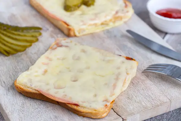 Zwei überbackene Scheiben Brot mit Schinken und Käse, garniert mit Gewürzgurken. Eine Karlsbader Schnitte, perfekt für einen herzhaften Snack.